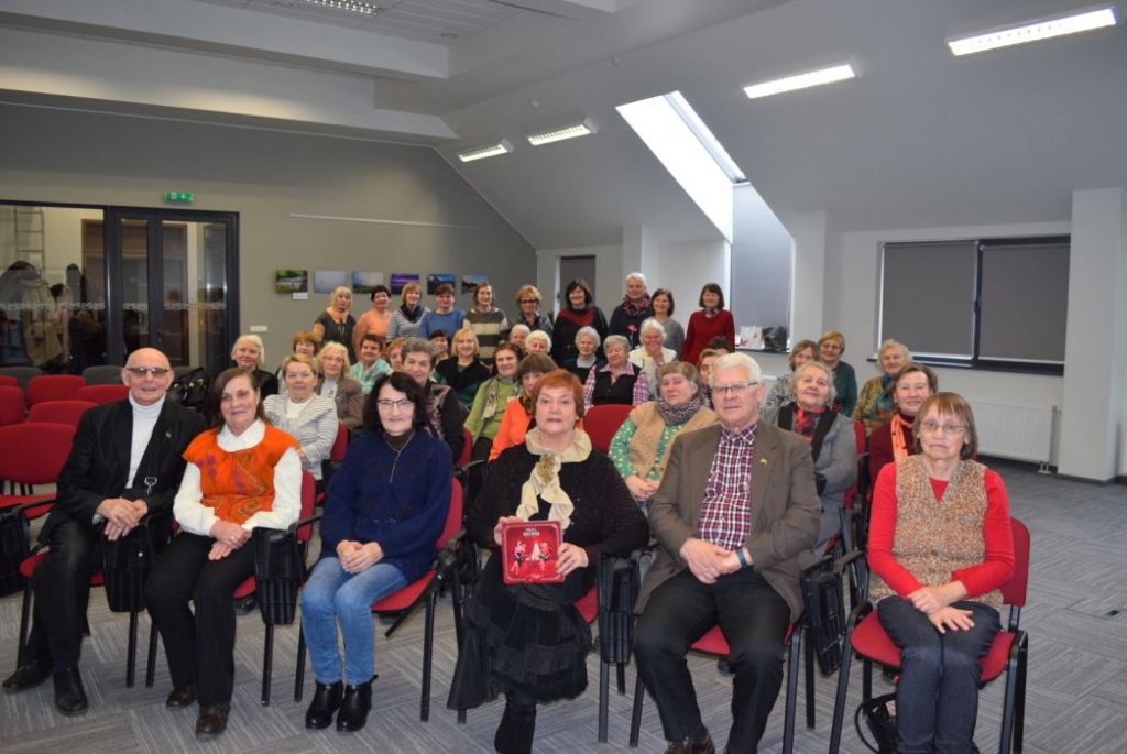 Žmonės susėdę salėje pozuoja fotografui