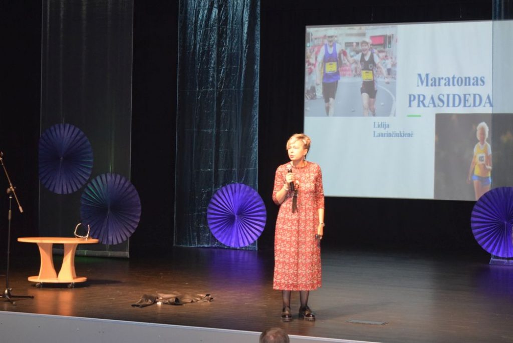 Scenoje lektorė L. Laurinčiukienė. Jai už nugaros ekrane užrašas „Maratonas prasideda“
