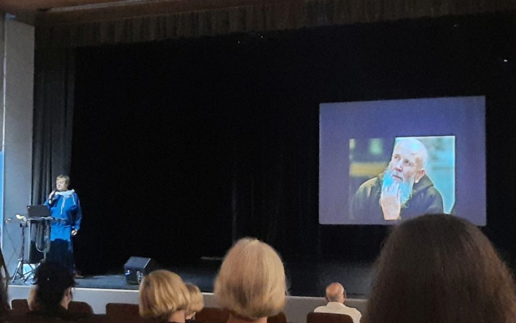 Salės vaizdas, scenoje matyti lektorė V. Bakutienė, ekrane - tėvas Stanislovas