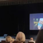 Salės vaizdas, scenoje matyti lektorė V. Bakutienė, ekrane - tėvas Stanislovas