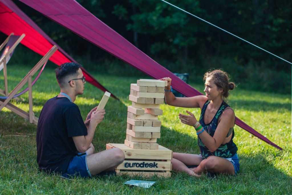 Du jaunuoliai - vaikinas ir mergina, sėdintys ant žodės ir dėliojantys jengos kaladėles ant dėžės su pavadinimu EURODESK