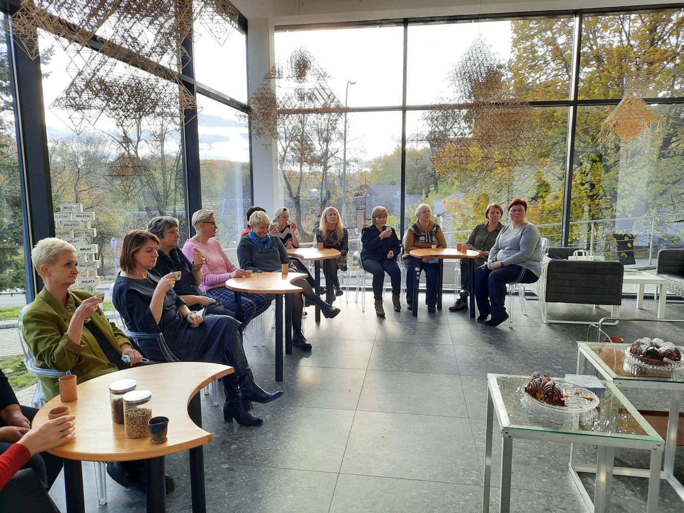 Mokytojai, sėdintys prie staliukų, dalyvaujantys kavos edukacijoje