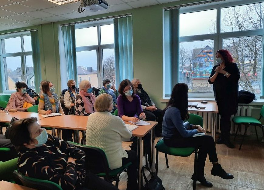 Žmonės, susėdę salėje ir besiklausantys lektorės paskaitos