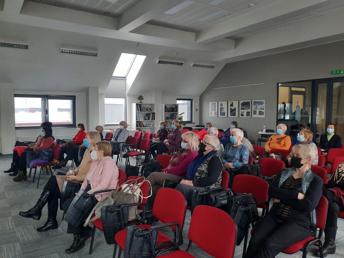 Žmonės, sėdintys salėje ir besiklausantys paskaitos