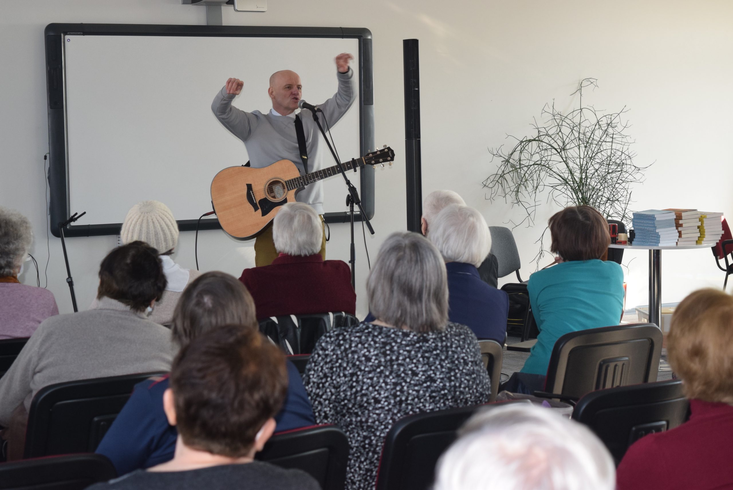 Žmonės, susėdę salėje, klausosi paskaitos