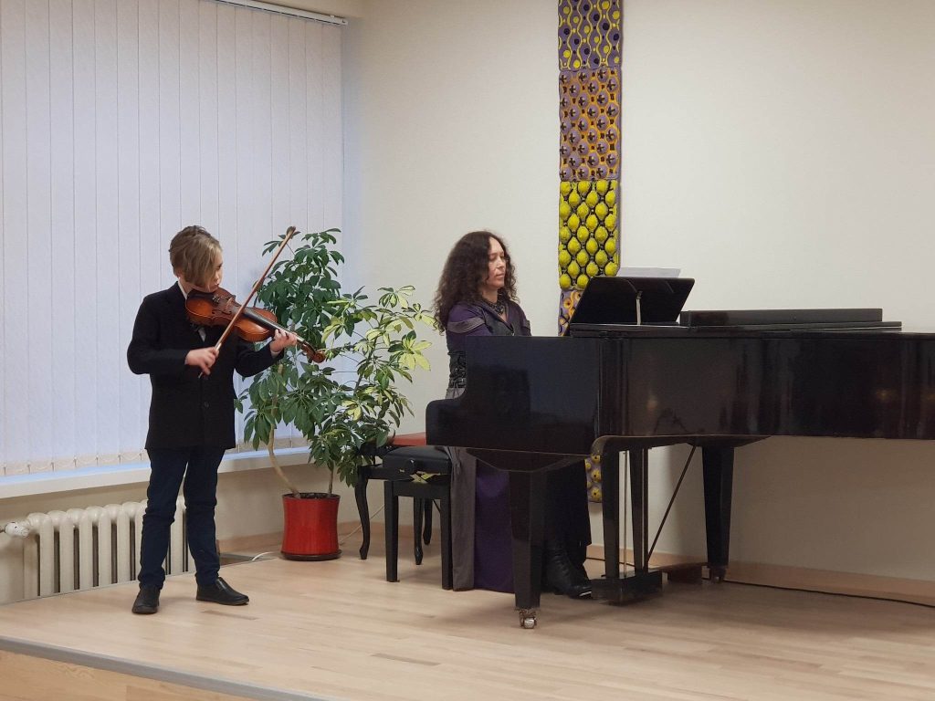 Mokinys groja smuiku. Mokytoja akomponuoja.