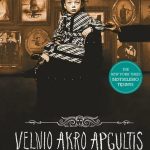mergaitė sėdi ant krėslo, už jos ant sienos kabo senovinės nuotraukos
